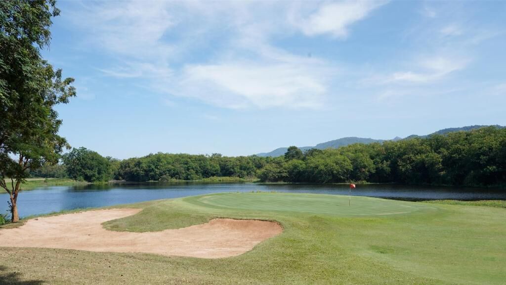 A golf course with a water body, trees, and a distant mountain range.
