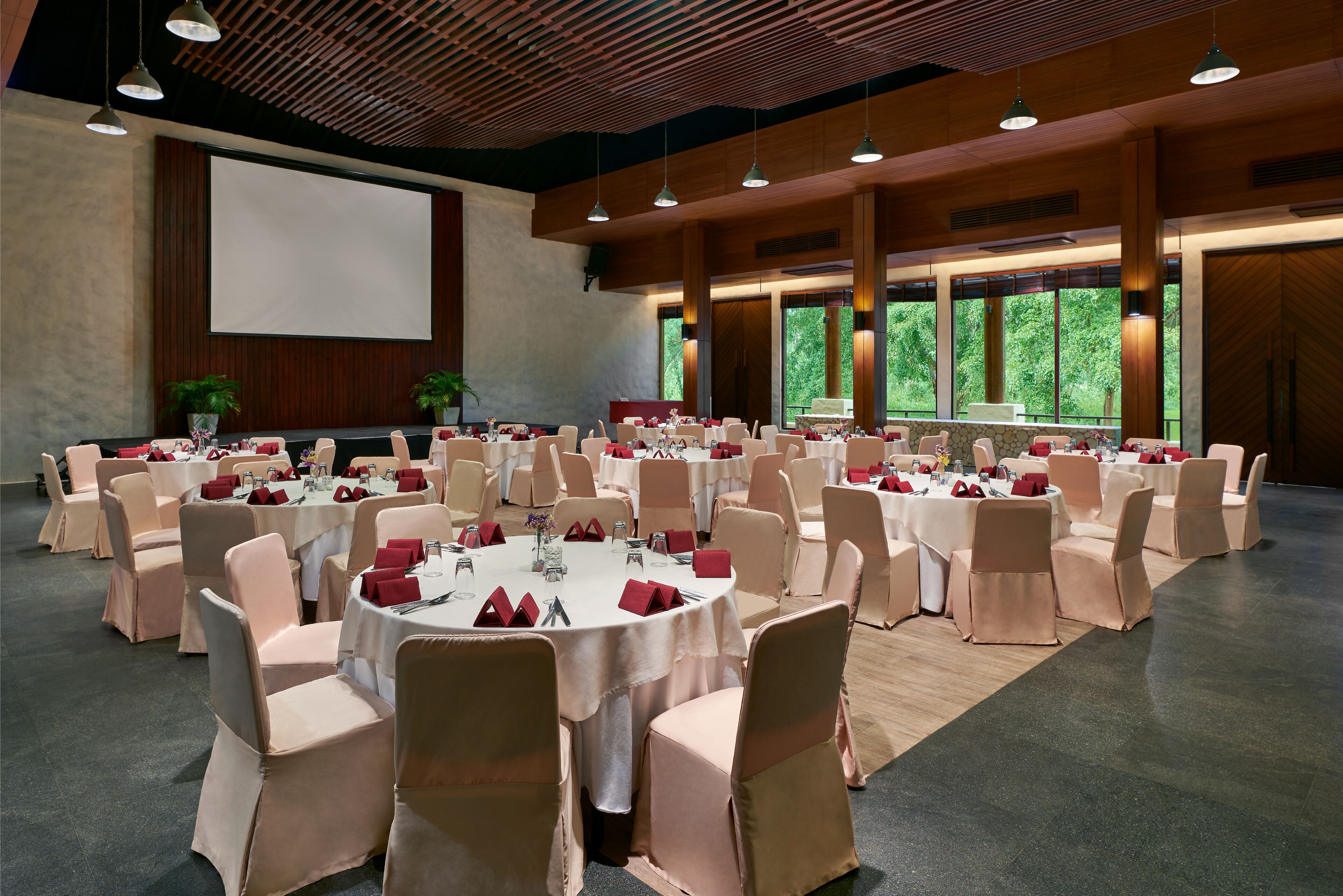 A large conference room with round tables, beige chairs, and red napkins.