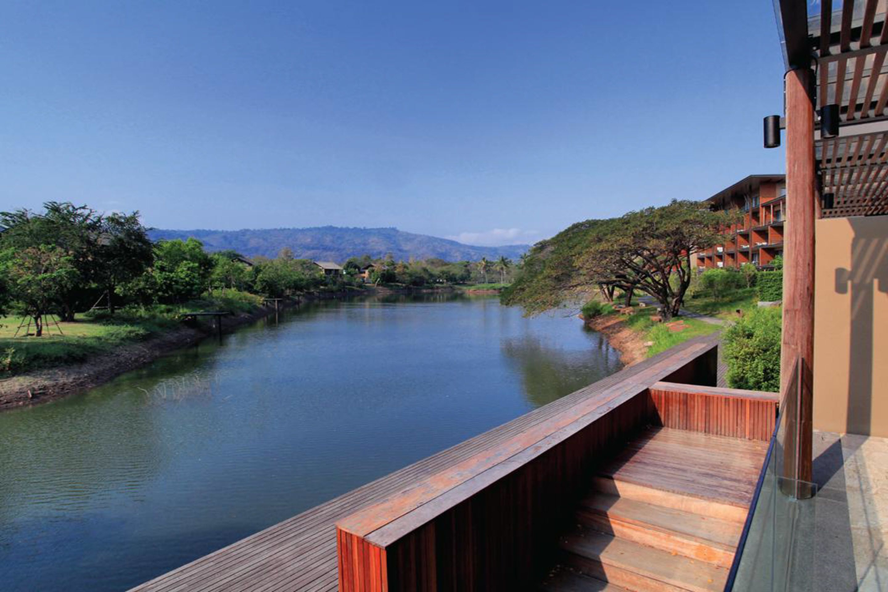 A wooden deck overlooking a calm river with a view of distant hills and a building with a traditional roof.