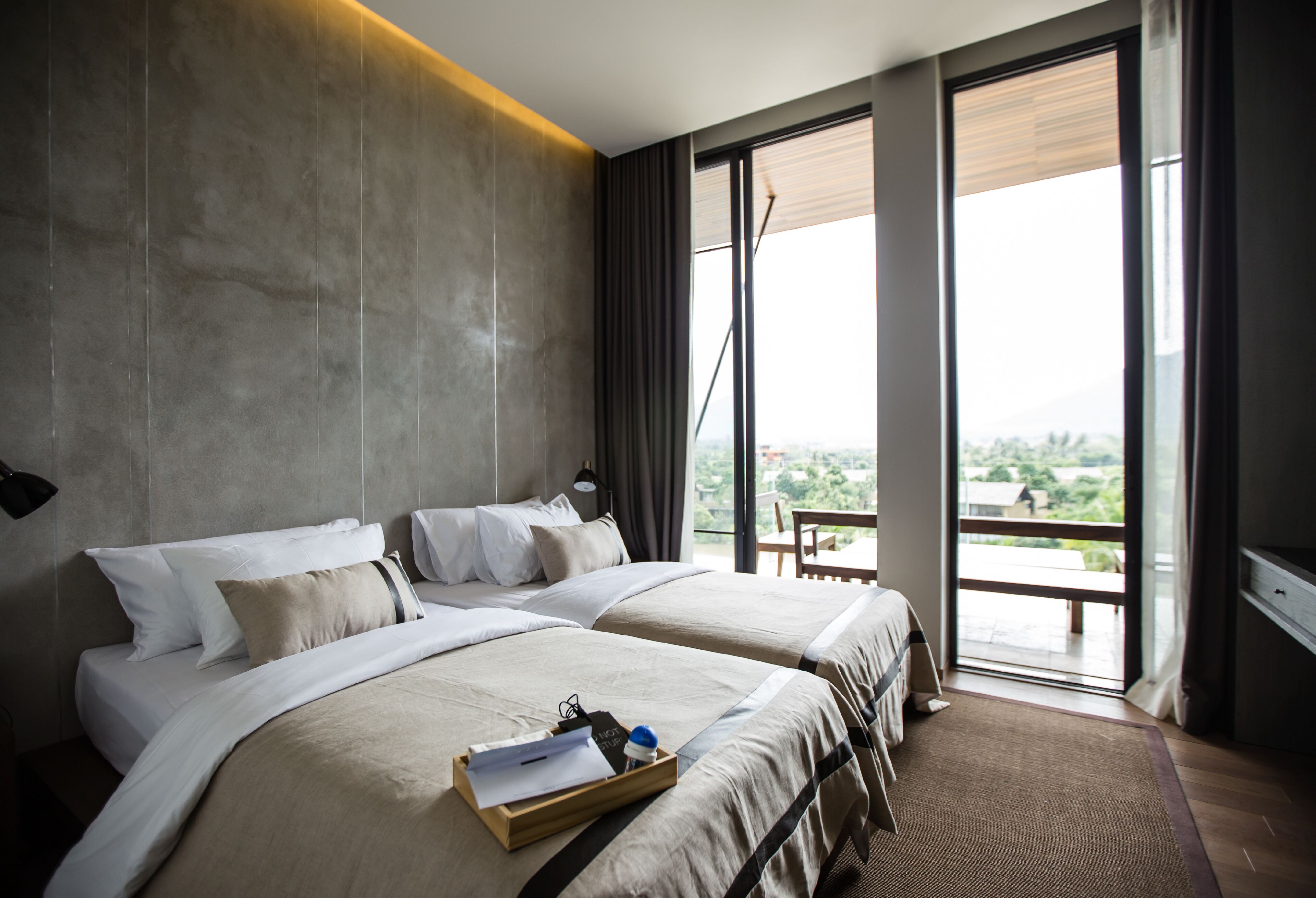 A hotel room with two beds, a large window with a view, and a balcony.
