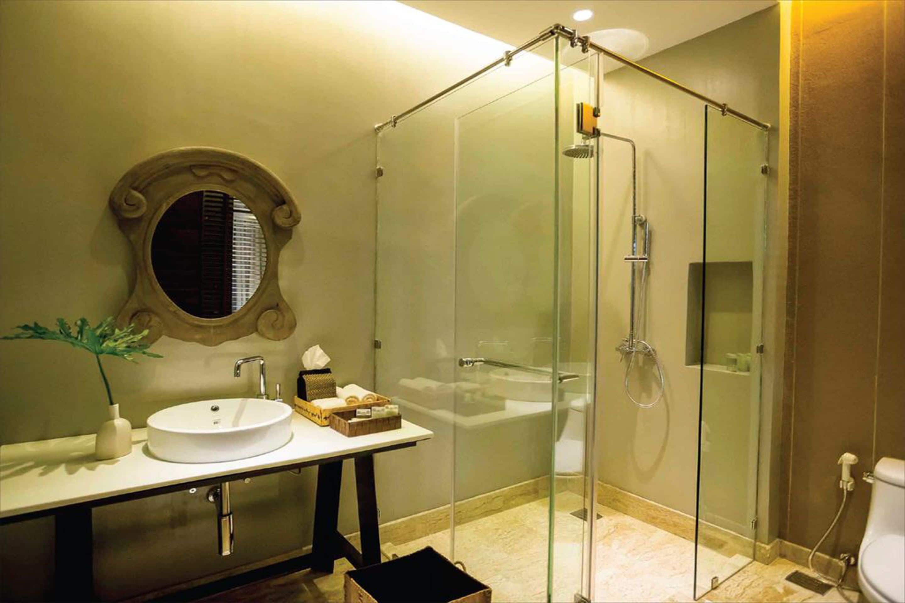 Une salle de bain moderne avec une douche à parois de verre, un miroir rond et un lavabo blanc.