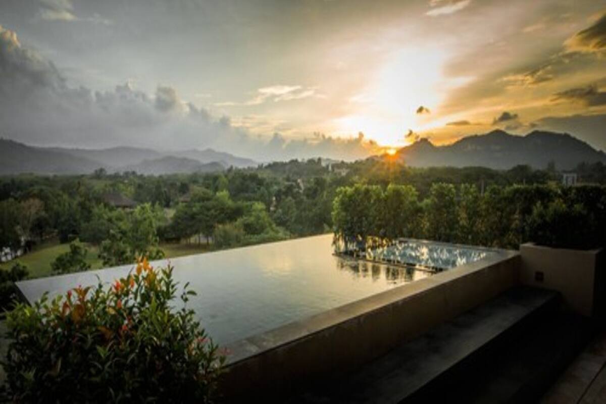 A rooftop infinity pool with a view of a sunset over a mountainous landscape.