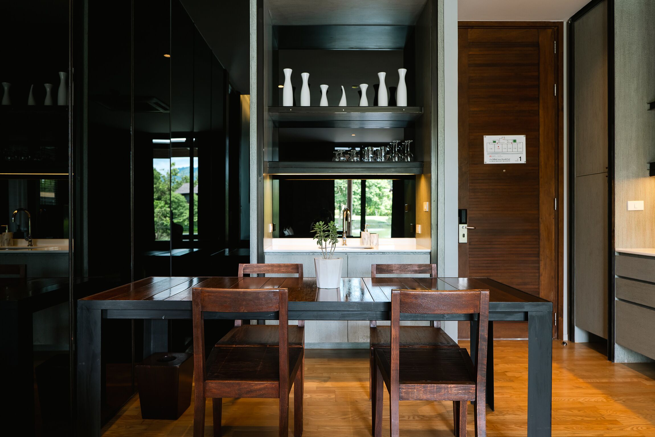 A modern kitchen with a wooden dining table and chairs, a built-in wine rack, and a view of the outdoors.