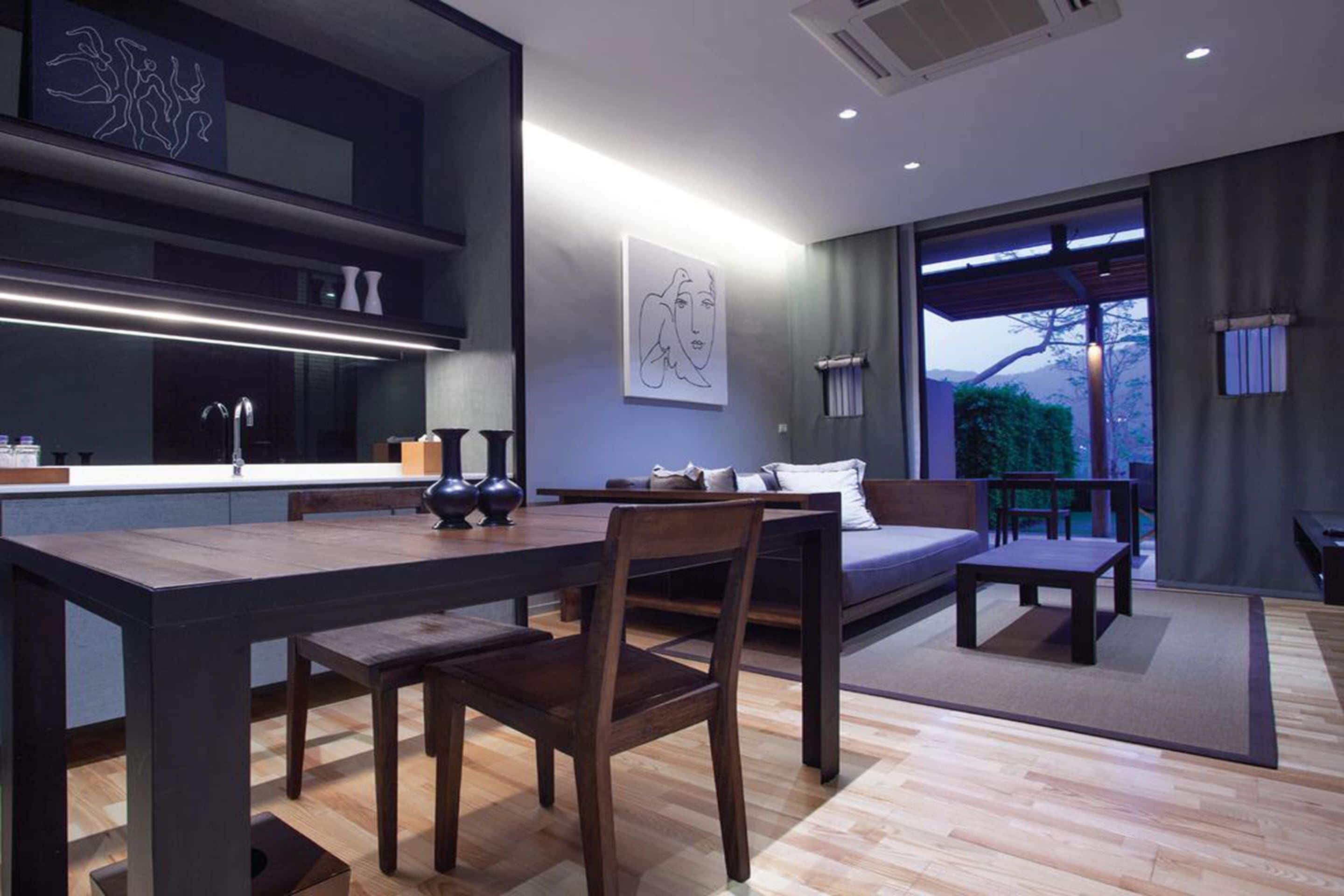 A modern interior with a dining area, a sofa, and a view through large windows.