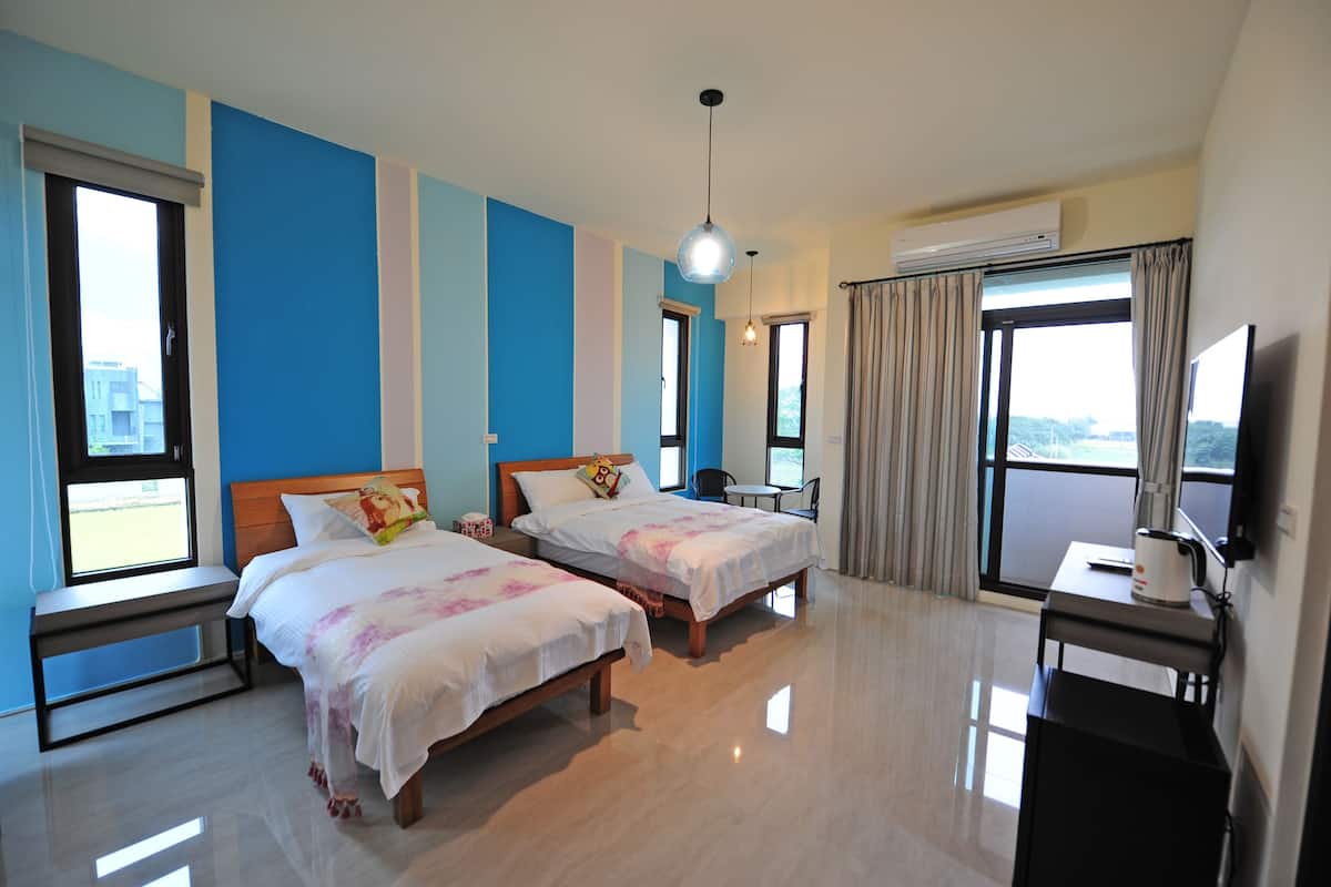 A hotel room with two beds, a TV, a desk, and a window with curtains.