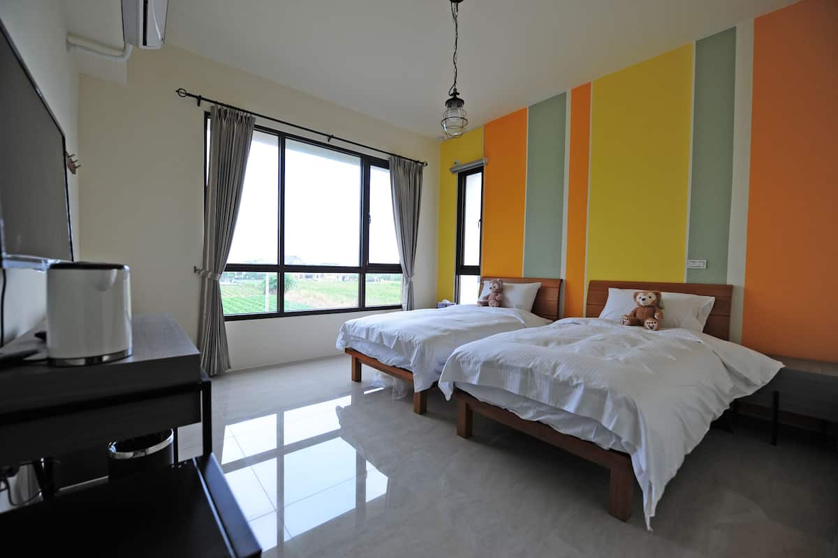 A hotel room with two beds, a desk with a coffee maker, and a large window with curtains.