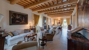 A spacious living room with a high wooden ceiling, a fireplace, and a large painting on the wall. - Relais Il Margarito (Montefano)