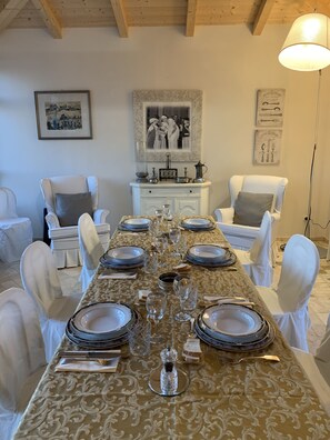A dining room with a long table set for a meal, surrounded by white chairs. - Relais Il Margarito (Montefano)