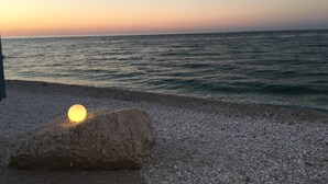 A pebbled beach with a large rock and a glowing light source, overlooking a calm sea at sunset. - Relais Il Margarito (Montefano)