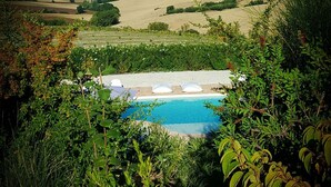 A pool surrounded by lush greenery, with a view of rolling hills and fields in the distance. - Relais Il Margarito (Montefano)