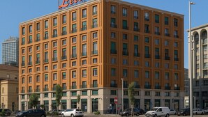 Een meerlaags hotel met een opvallend 'Lete'-bord, met een raster van ramen en balkons, gelegen in een stedelijke omgeving met nabijgelegen gebouwen.
