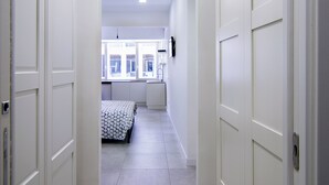 Een smalle gang met witte deuren die leiden naar een slaapkamer en een keuken.