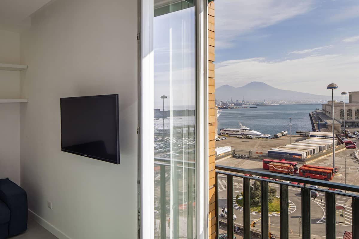A balcony with a TV, a view of a harbor with boats, and a mountain in the distance.