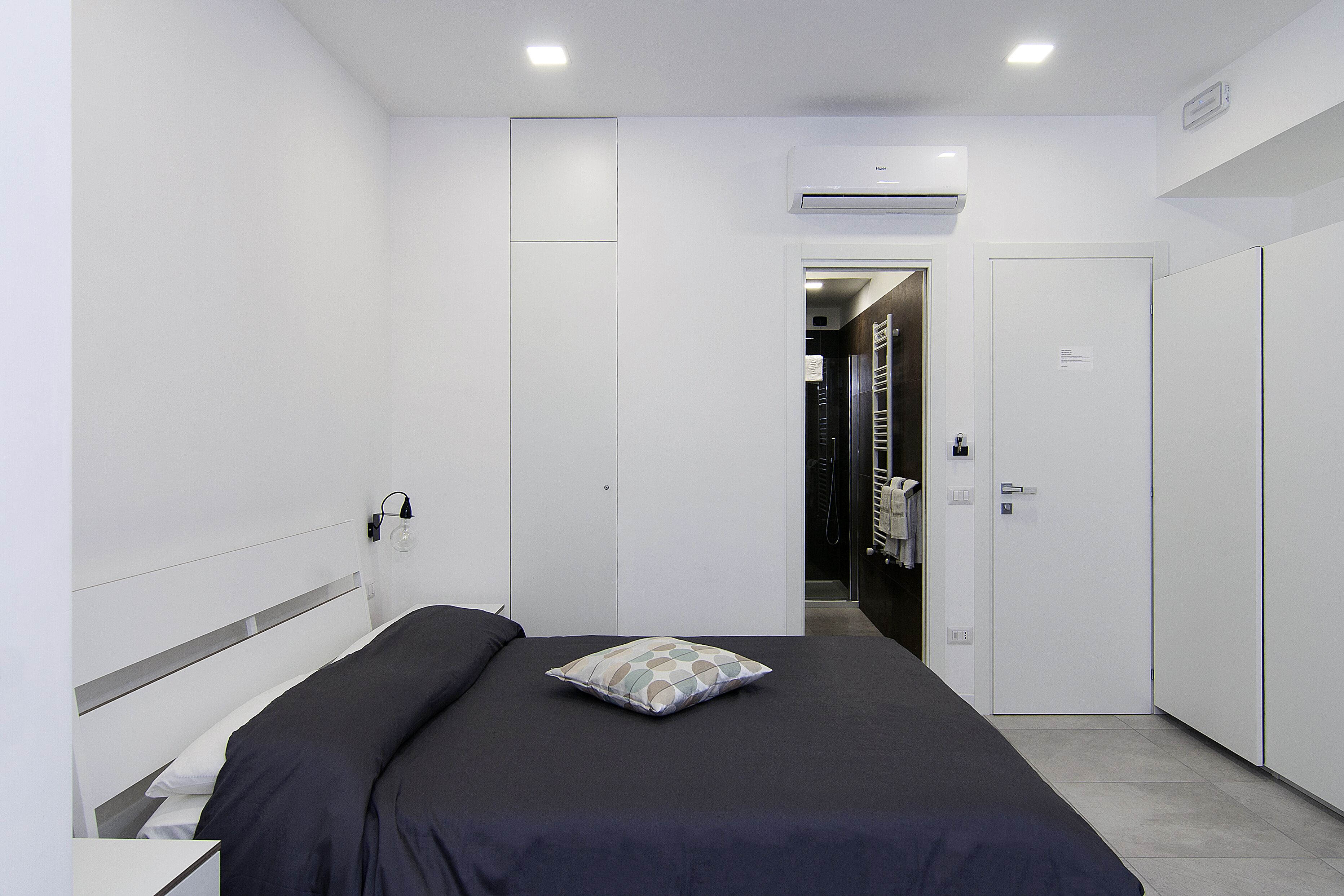 A modern bedroom with a bed, a pillow, a wardrobe, and a door leading to a hallway.