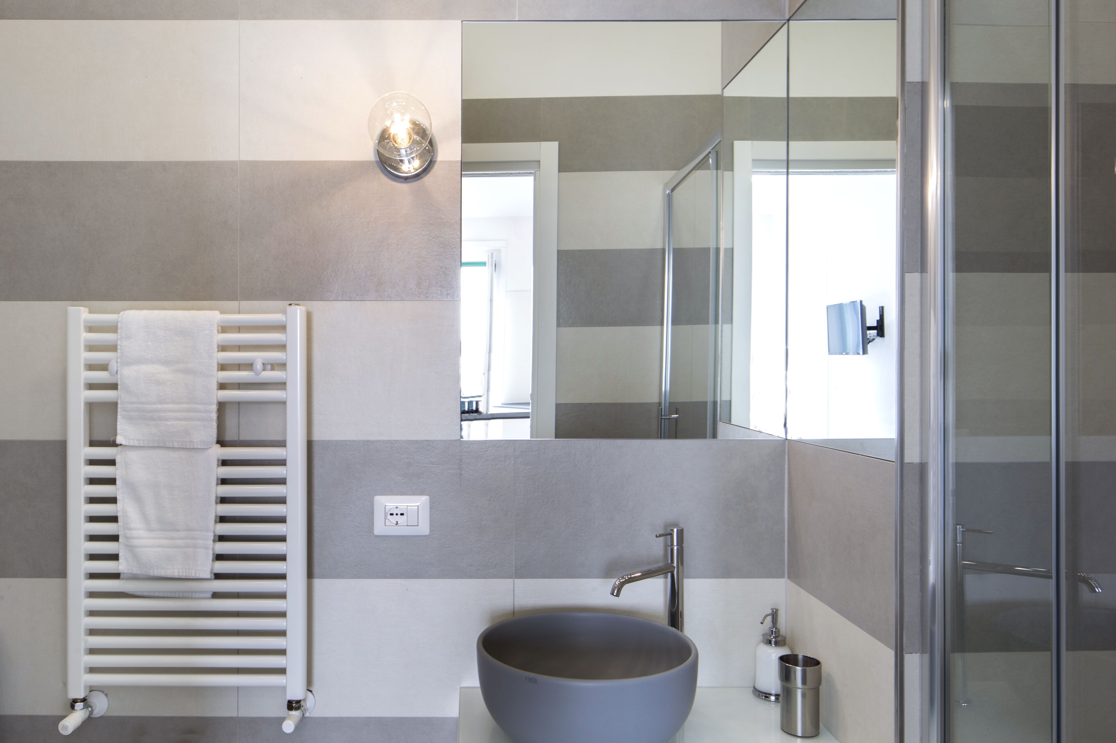 Un baño moderno con un lavamanos tipo recipiente, una cabina de ducha con mampara de vidrio y un perchero con toallas blancas.
