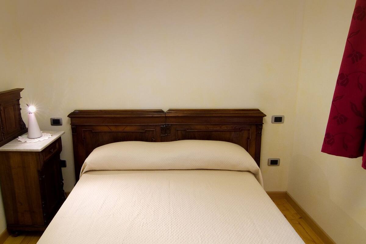 A bedroom with a wooden headboard, a bedside table with a lit candle, and a red curtain.