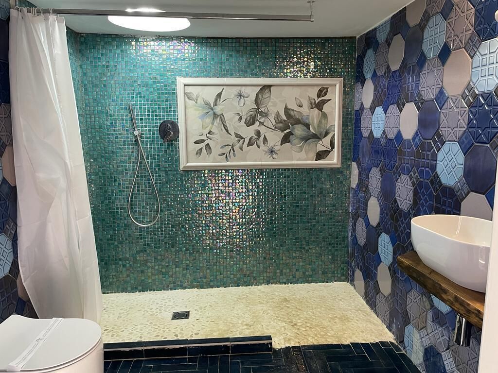 Un baño con ducha, un cuadro floral enmarco, un lavabo y una pared de mosaico.