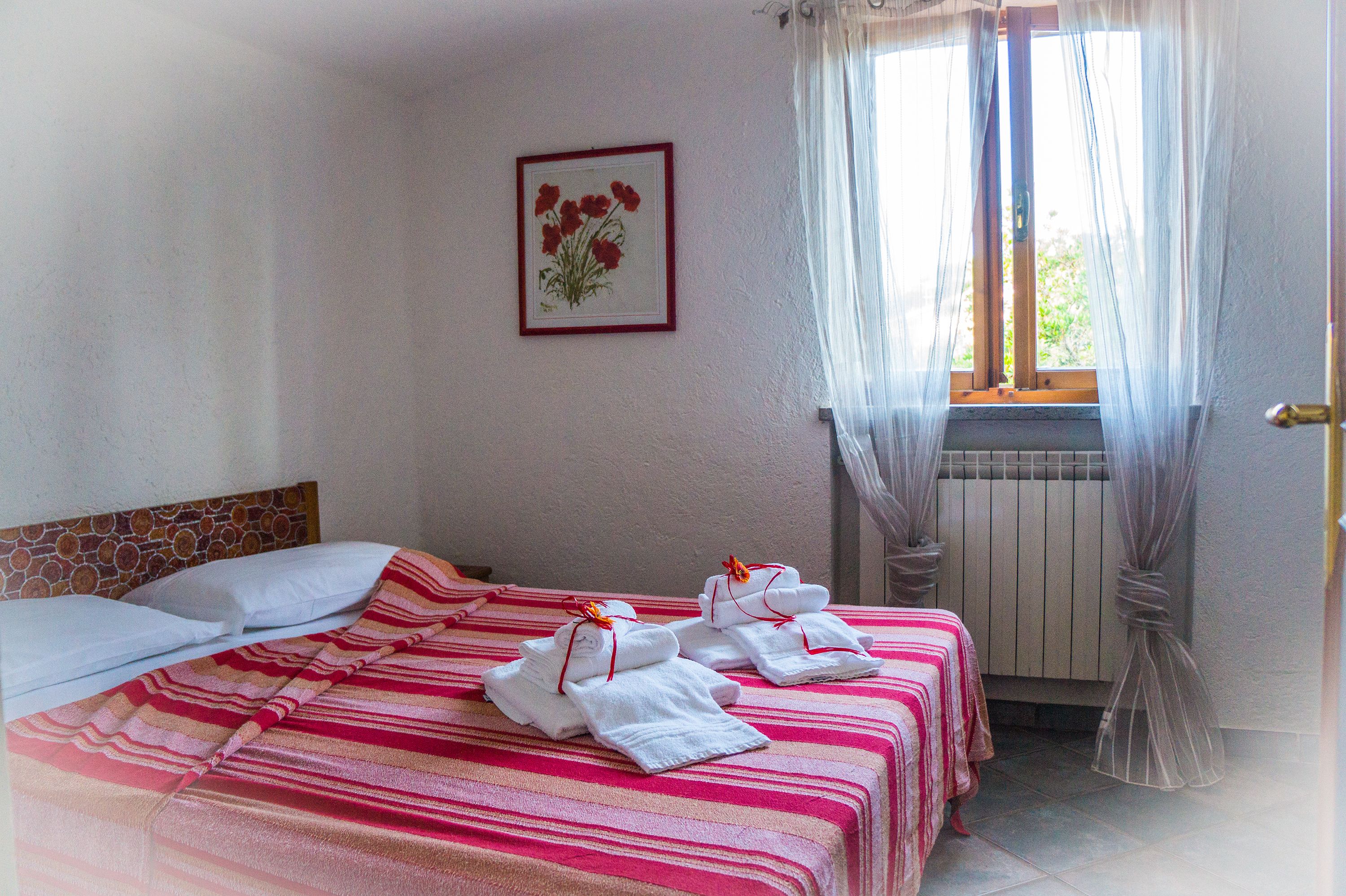 Habitación de hotel con cama, ventana con cortinas translúcidas, radiador y un cuadro en la pared.