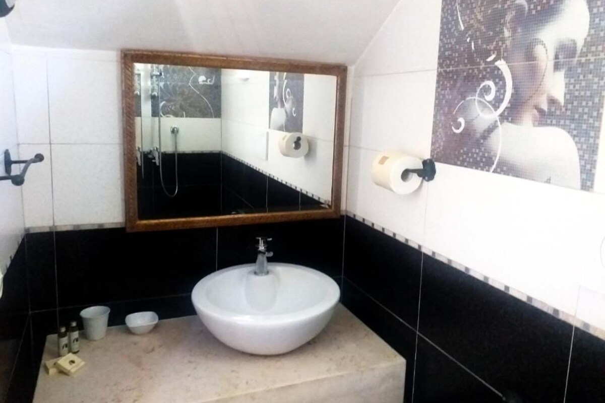 A bathroom with a white sink, a mirror, a towel dispenser, and a toilet paper holder.