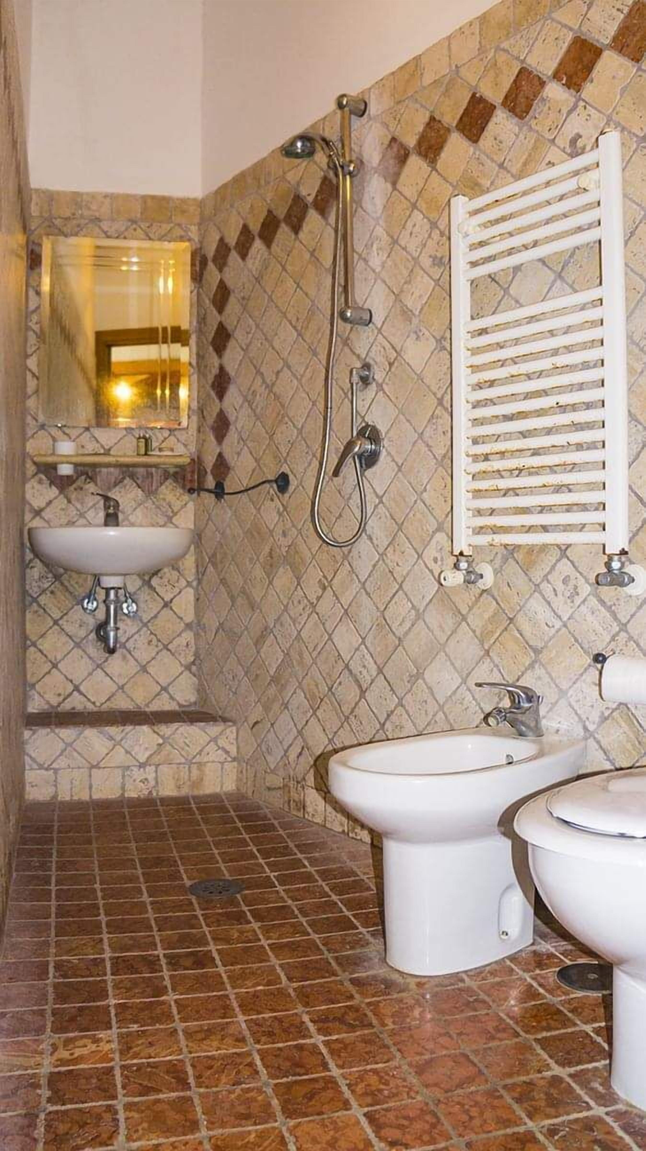 A bathroom with a tiled floor, a sink, a bidet, a shower, and a towel rack.