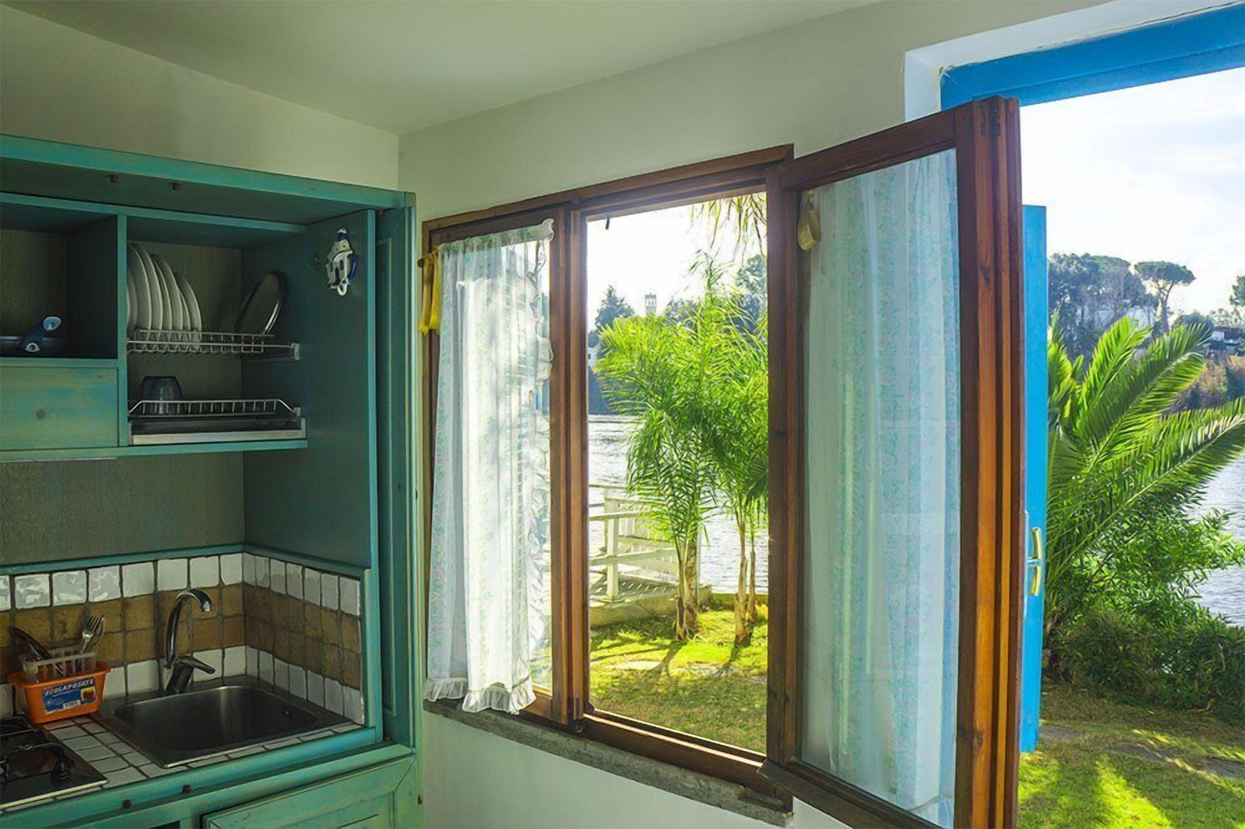 A kitchen with a window view of a garden and a body of water.