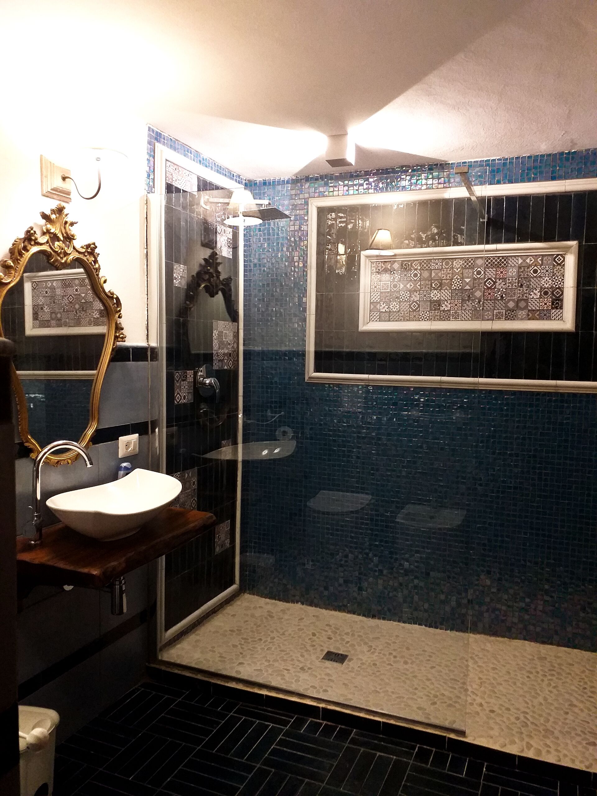A bathroom with a white sink, a mirror with an ornate frame, and a shower area with blue mosaic tiles.