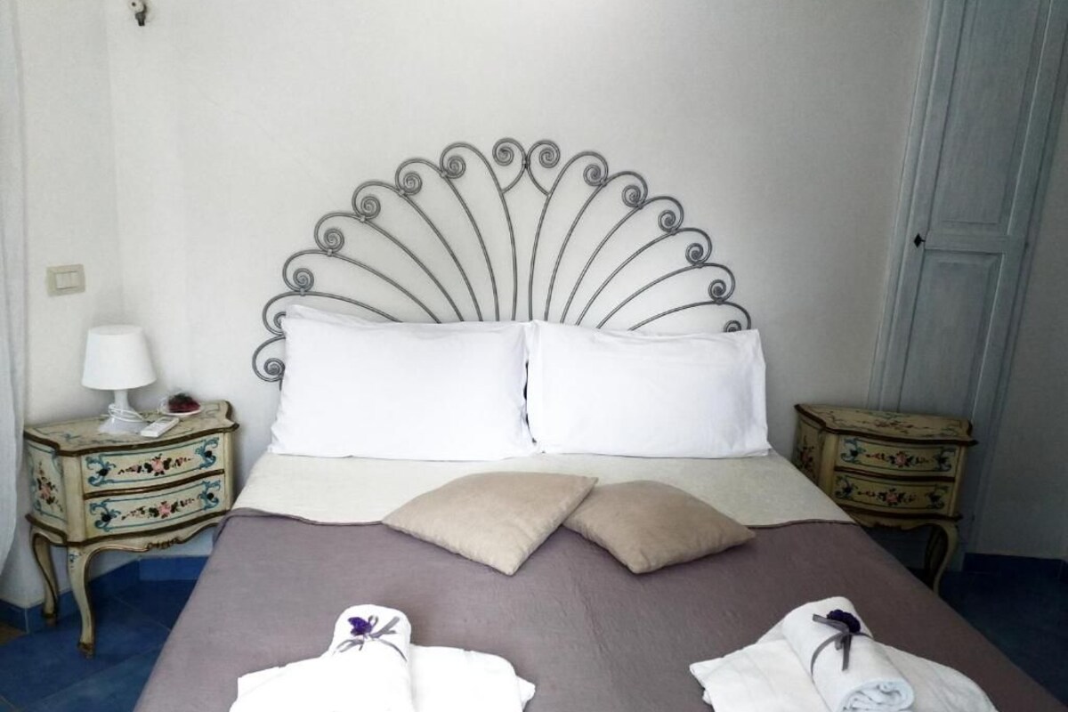 A neatly made bed with a metal headboard, two bedside tables with lamps, and a door in the background.