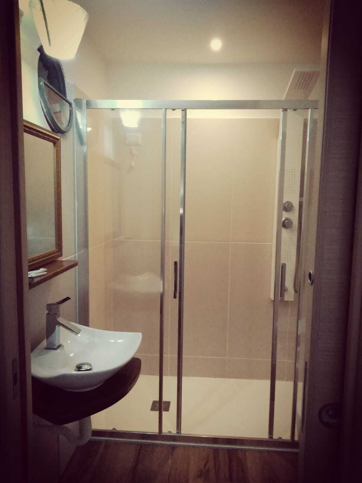 A bathroom with a glass-enclosed shower, a sink with a mirror above it, and a wooden floor.