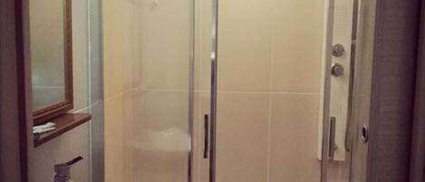A bathroom with a glass-enclosed shower, a sink with a mirror above it, and a wooden floor.