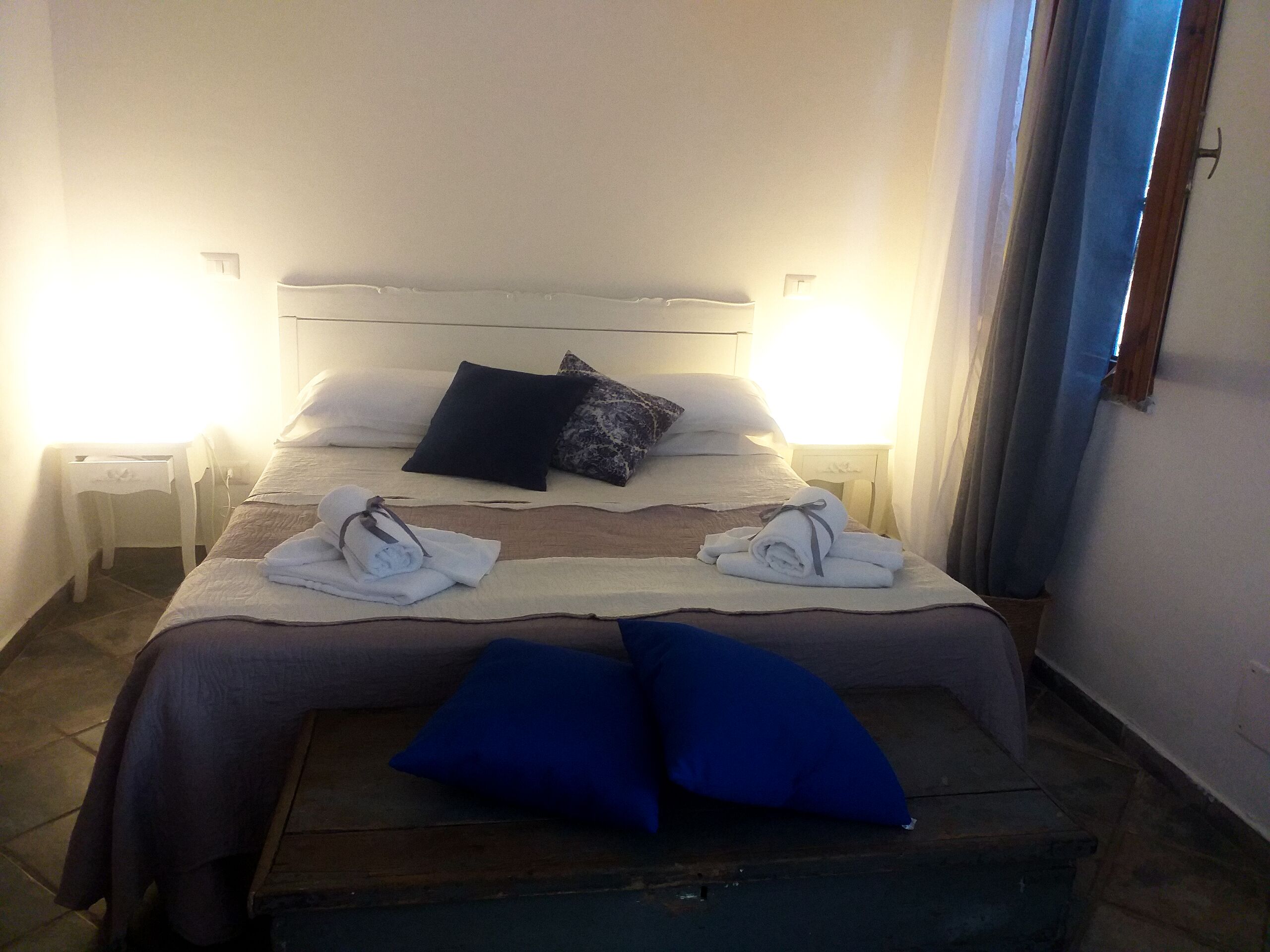 Una cama bien hecha con almohadas, una mesita de noche y un banco al pie de la cama.