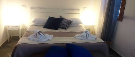 Una cama bien hecha con almohadas, una mesita de noche y un banco al pie de la cama.
