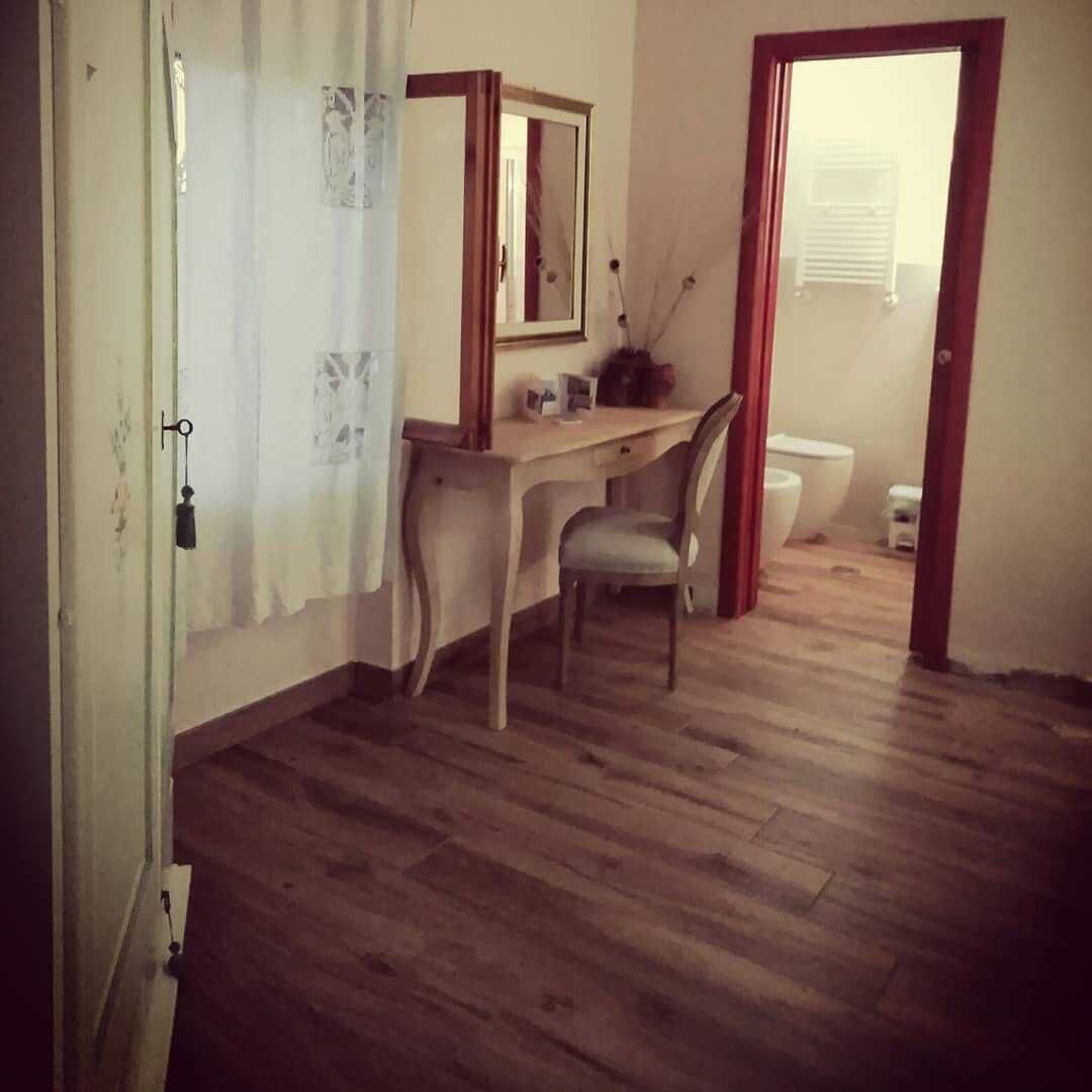 Una habitación con piso de madera, un escritorio con silla, un espejo y un inodoro.