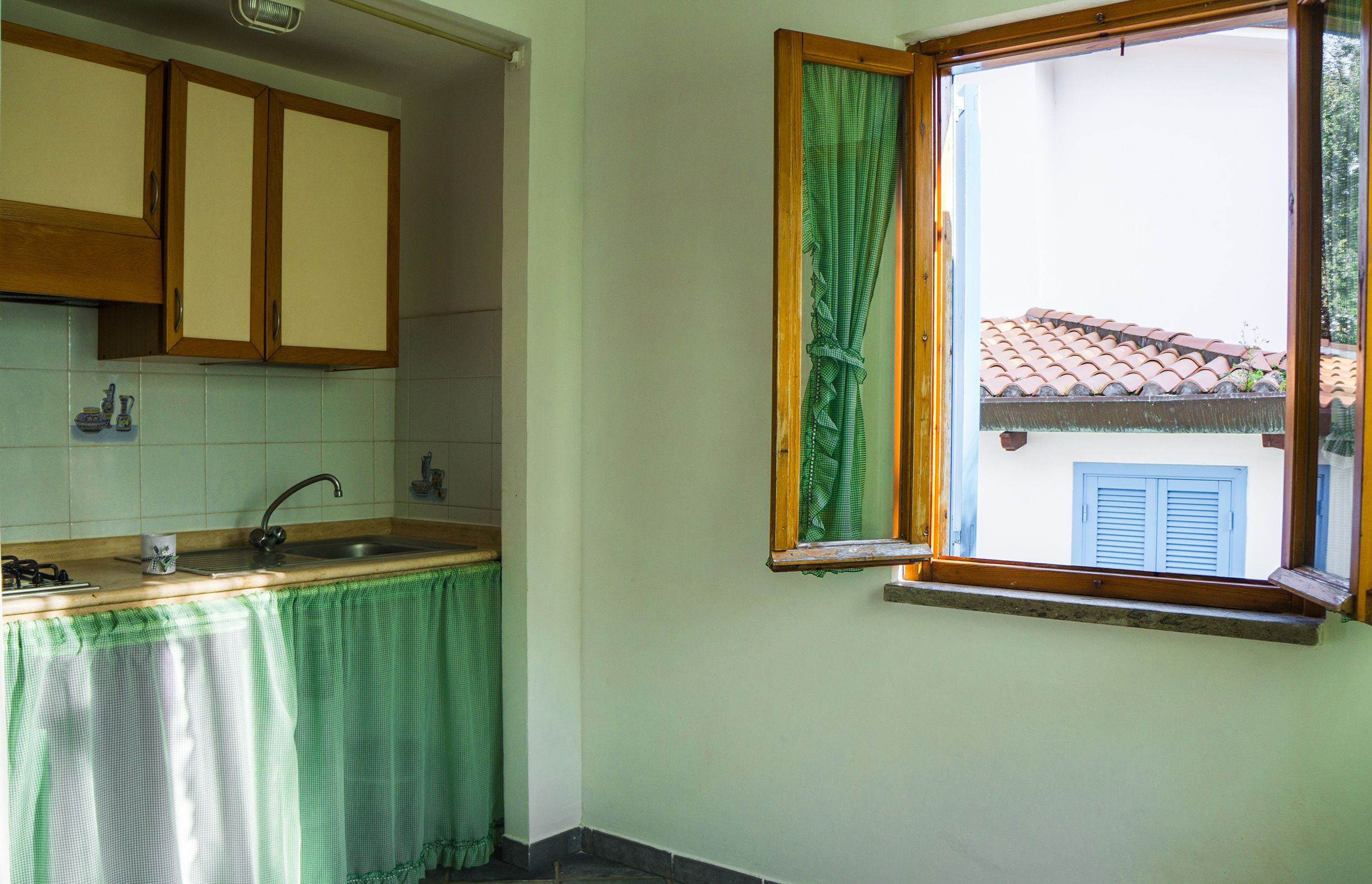 A kitchen with wooden cabinets, a sink, and a window with a green curtain.