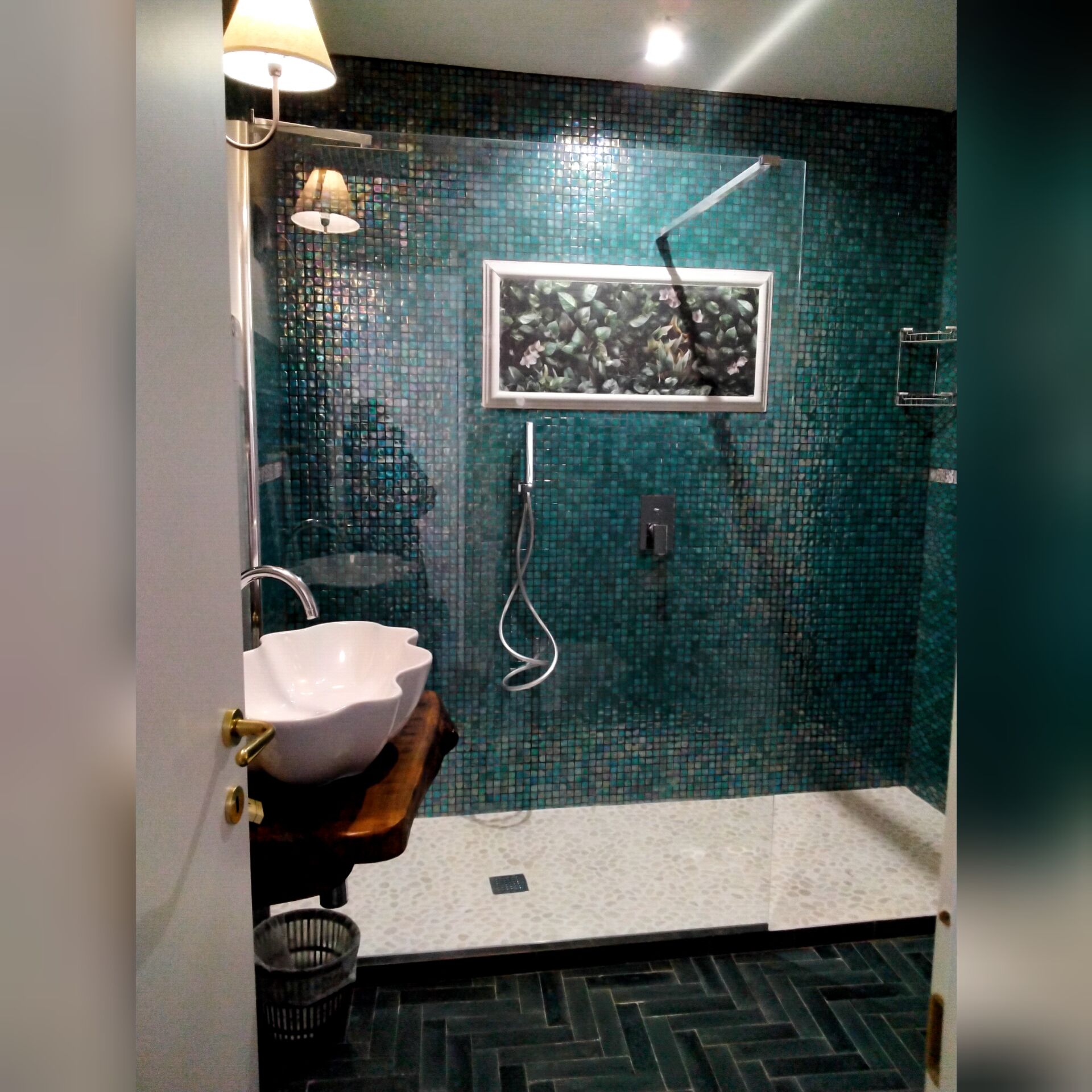 A bathroom with a mosaic tile wall, a white sink, a shower, and a herringbone floor pattern.