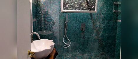 A bathroom with a mosaic tile wall, a white sink, a shower, and a herringbone floor pattern.