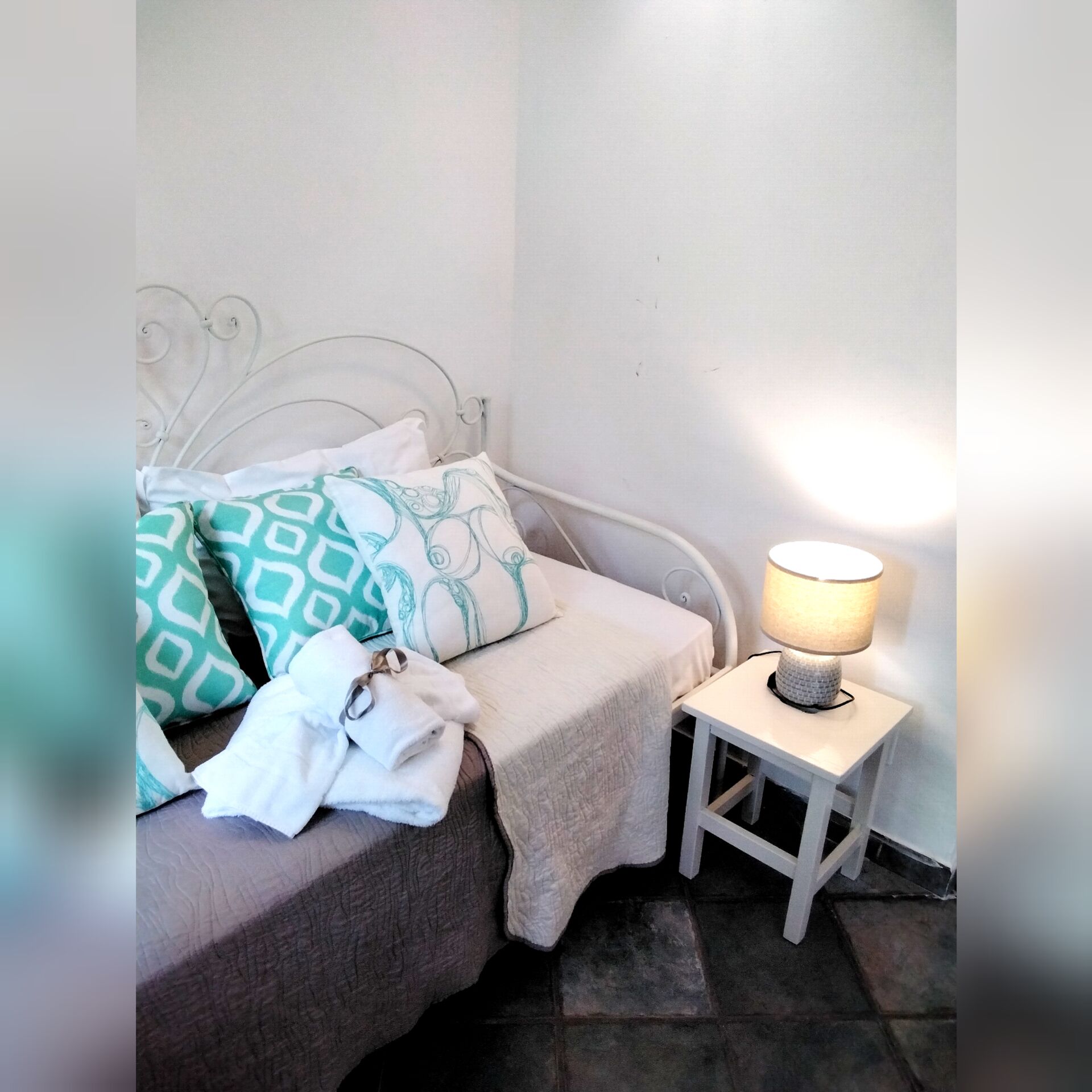 A bed with a white metal frame, a bedside table with a lamp, and patterned pillows.