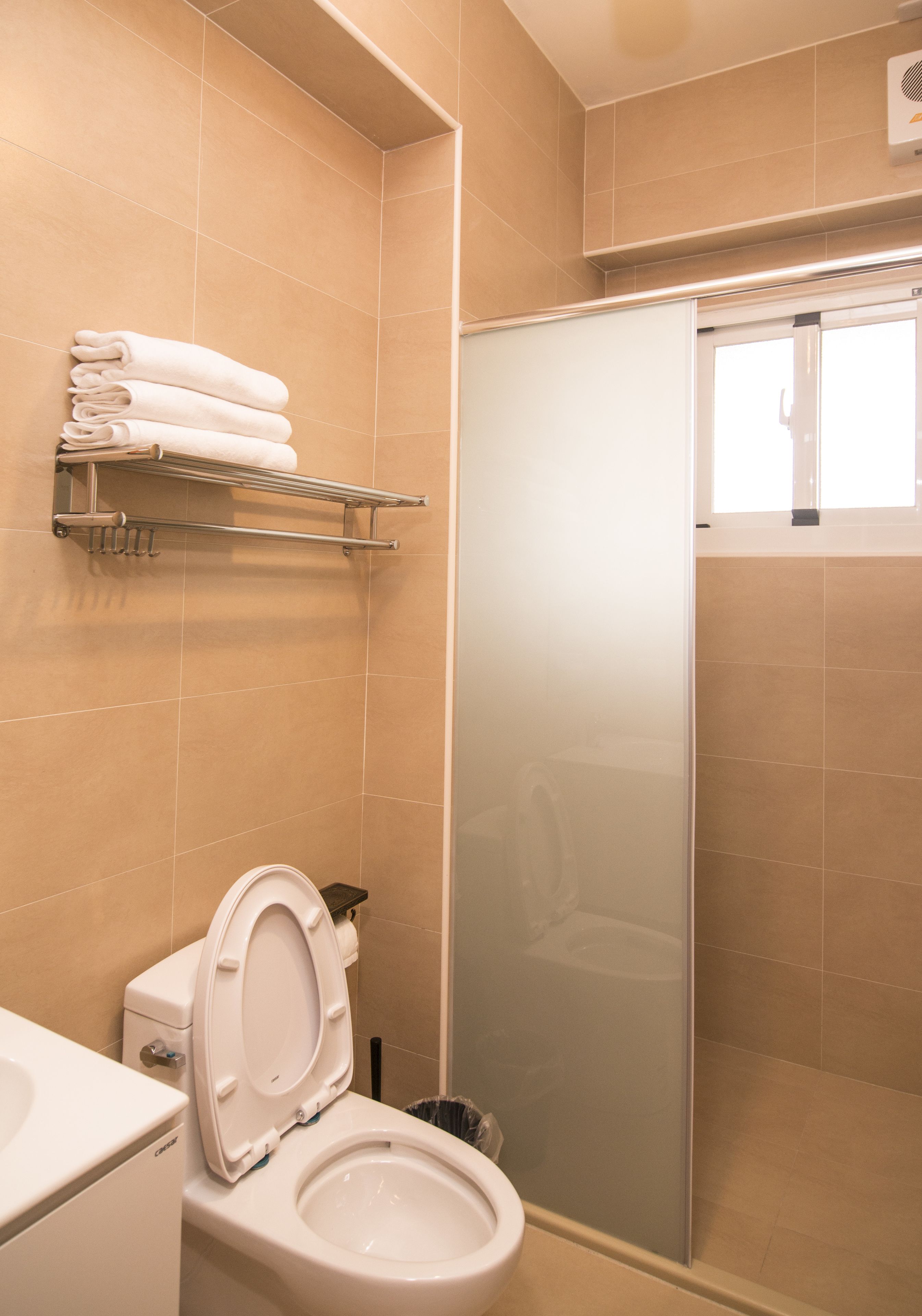 Un baño con inodoro, cabina de ducha de vidrio y toallero con toallas dobladas.