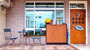 Una puerta de madera con una decoración de cabeza de ciervo, una ventana que ofrece vistas a edificios, y una mesa con sillas afuera.