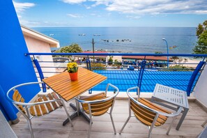 A balcony with a wooden table and chairs, a potted plant, and a view of the sea and beach. - La Favorita Hotel (Dorgali)