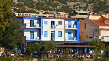 Un edificio a più piani con pareti esterne azzurre e bianche, un ristorante al piano terra e un muro di pietra in primo piano.