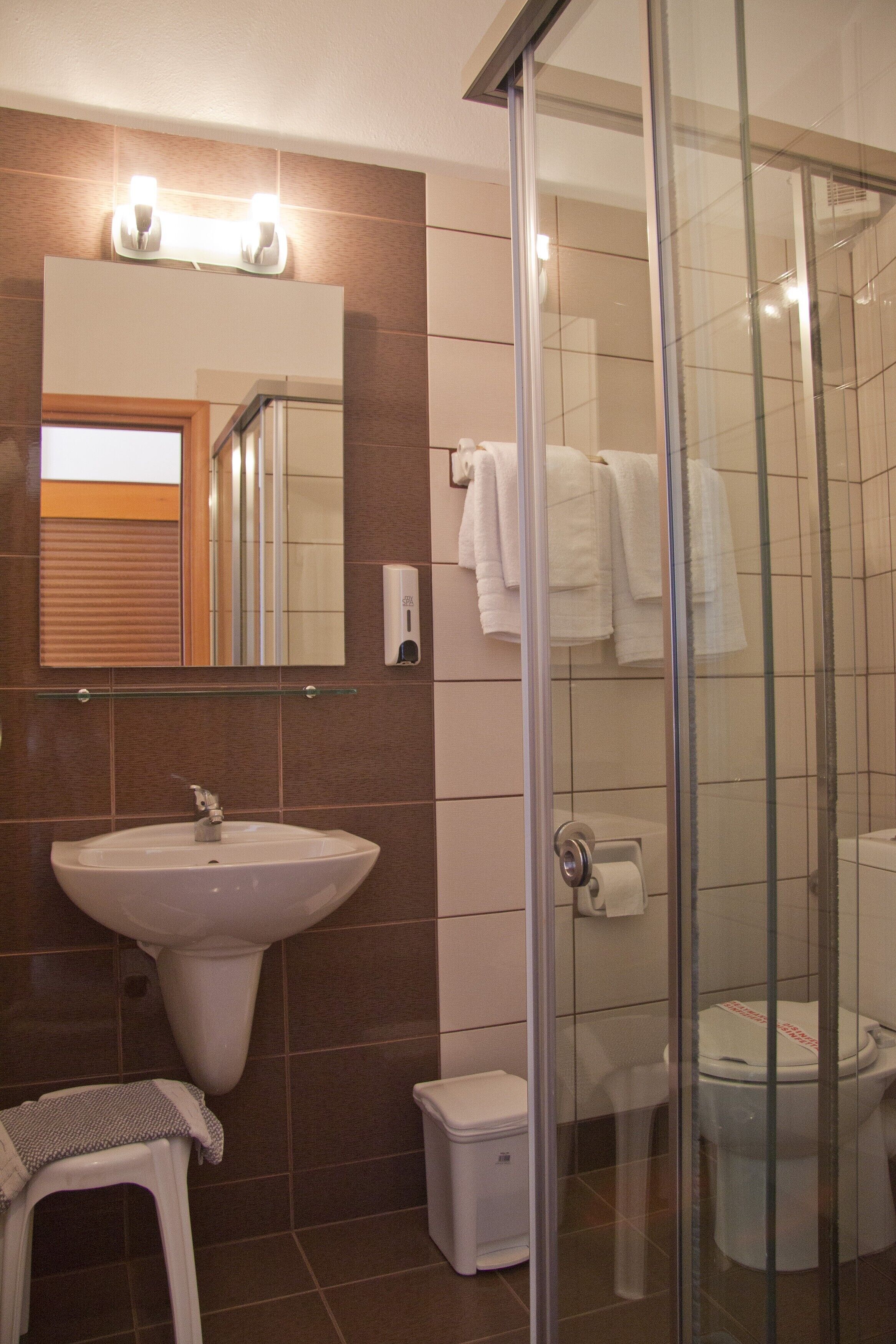 A bathroom with a sink, mirror, towel rack, glass shower enclosure, toilet, and a small stool.