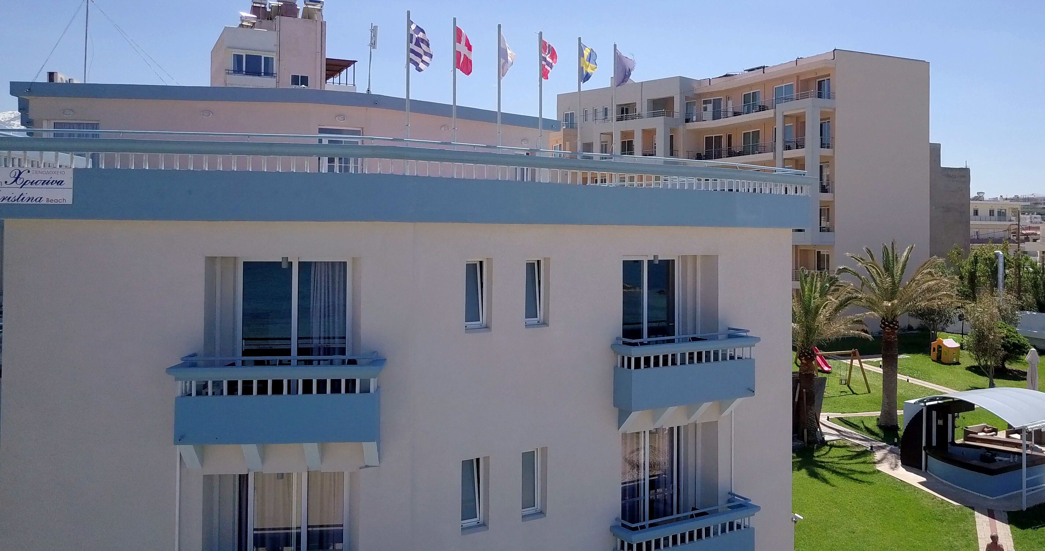 A multi-story hotel with balconies, a sign indicating a beach location, and multiple flags on the roof.