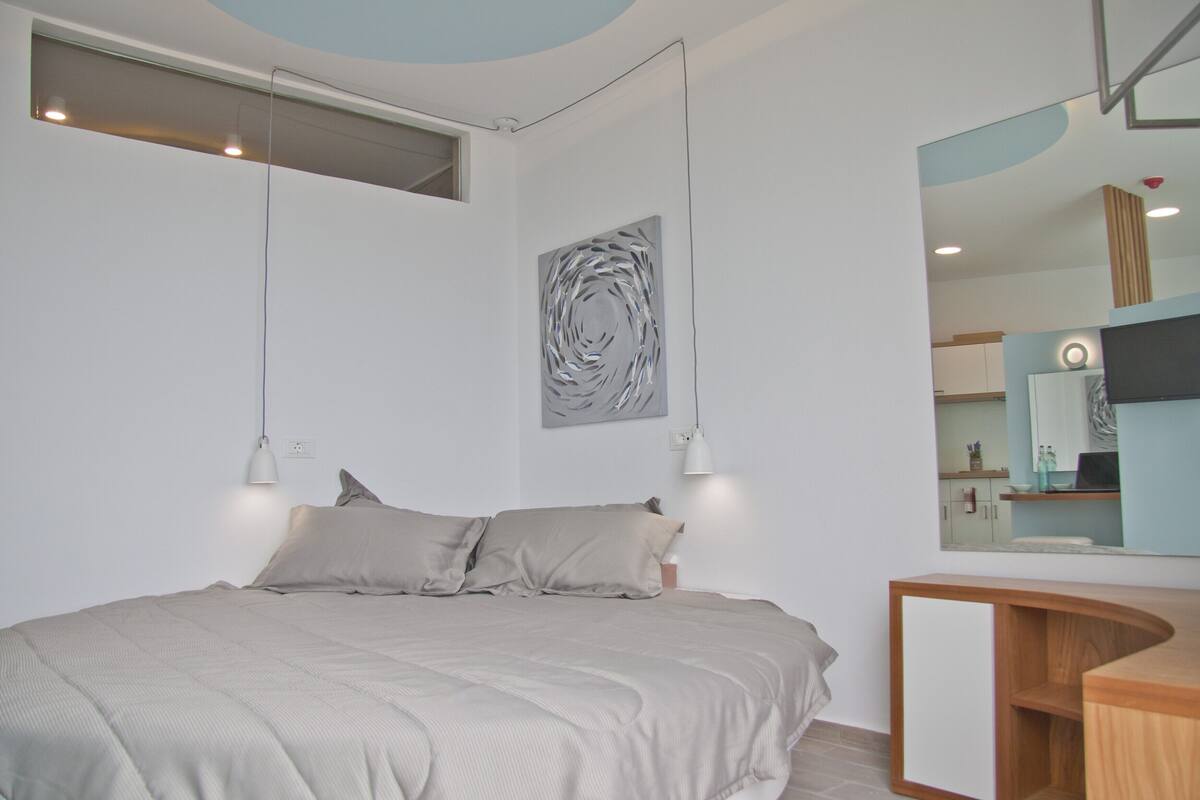 A modern bedroom with a bed, bedside lamps, a wall-mounted abstract art piece, and a built-in wooden desk.