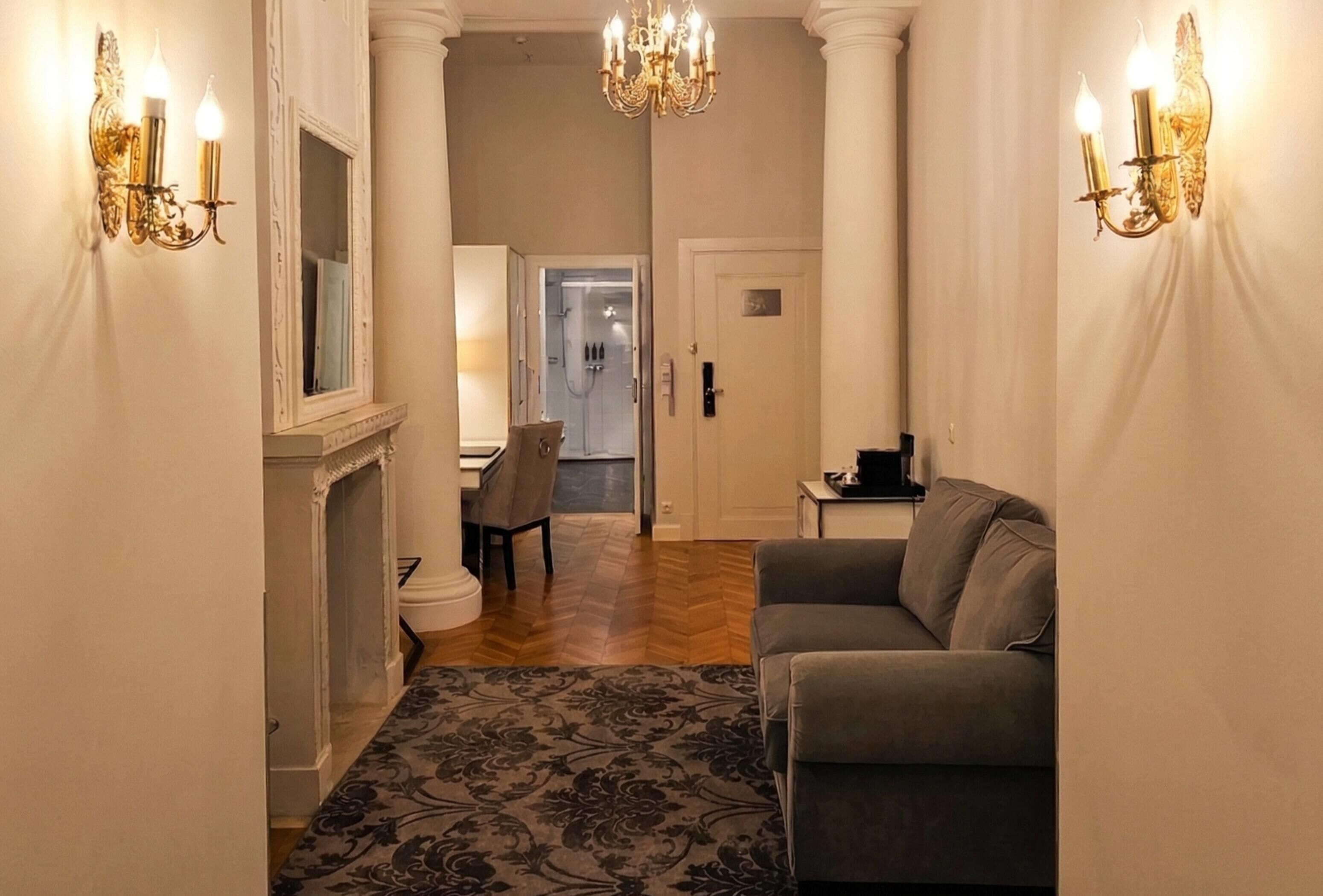 A hallway with a sofa, a chandelier, and wall sconces.