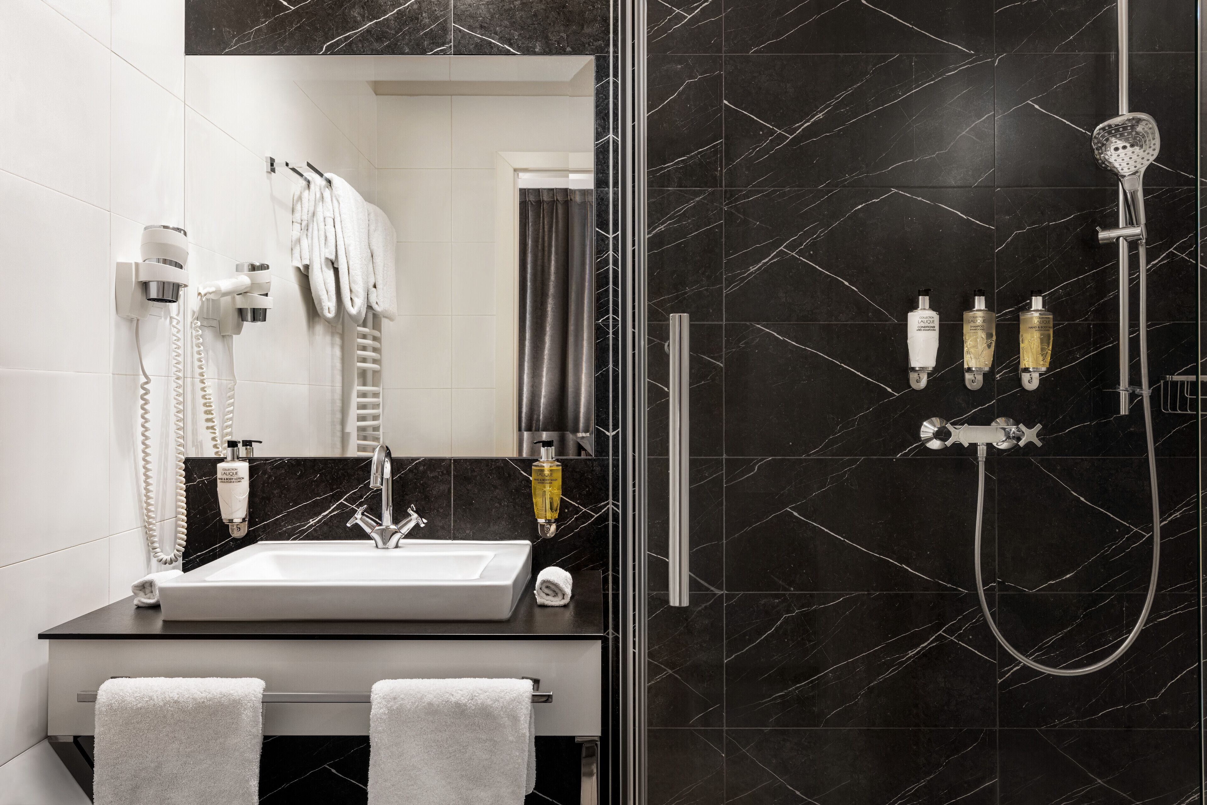 Un baño moderno con un espejo grande, un lavamanos, una ducha con cabezal de ducha manual y dos botellas de champú.