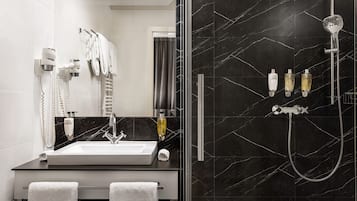 Un baño moderno con un espejo grande, un lavamanos, una ducha con cabezal de ducha manual y dos botellas de champú.