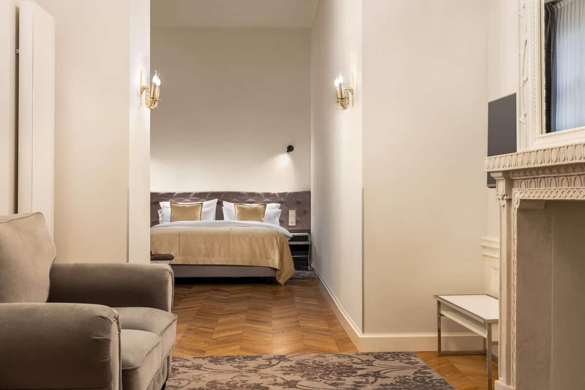 Kapea hotellihuone, jossa on sänky, sohva, pieni pöytä ja takka.