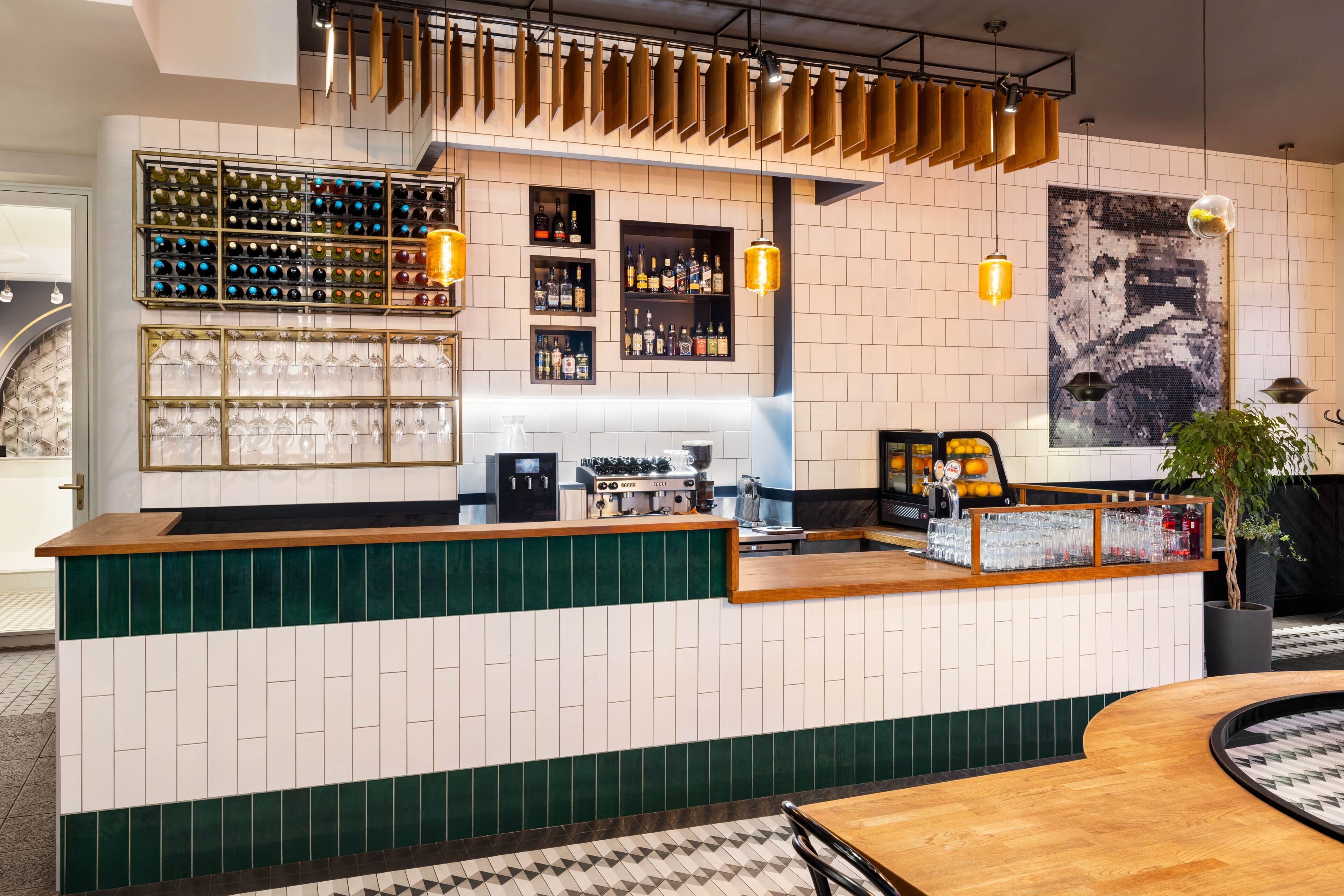 Uma área de bar com balcão, garrafas de vinho e bebidas alcoólicas, prateleiras e luminárias pendentes.