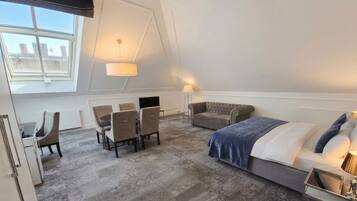 A hotel room with a bed, a sofa, a desk with chairs, a lamp, and a window.