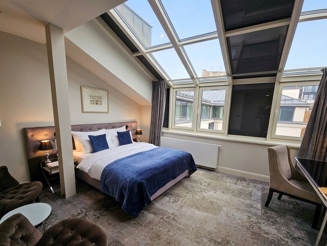 A hotel room with a bed, a desk, a chair, a small table, and a large skylight.